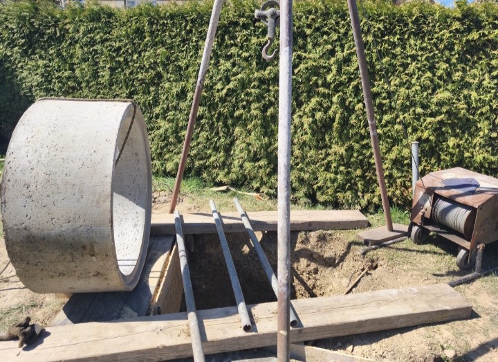 Betonová skruž položená vedle vykopané jámy, nad ní trojnožka s vrátkem