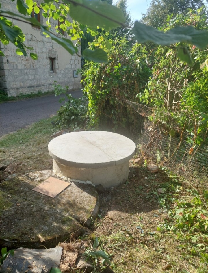 Kulaté betonové víko záhlaví studny v zahradě u kamenné budovy