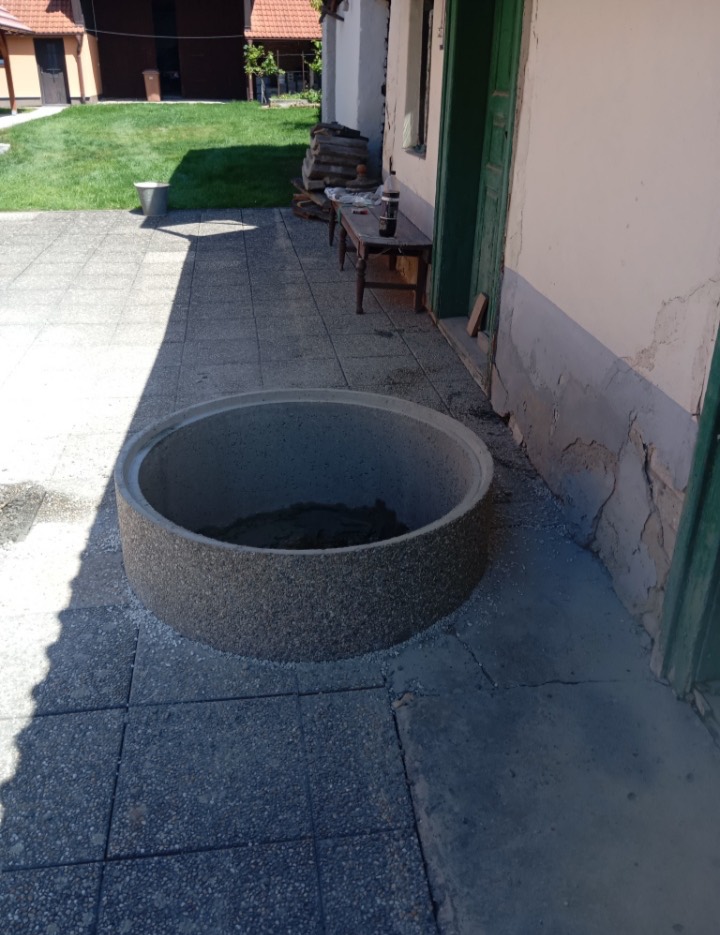 Betonová skruž osazená na dlažbě vedle domu jako záhlaví kopané studny