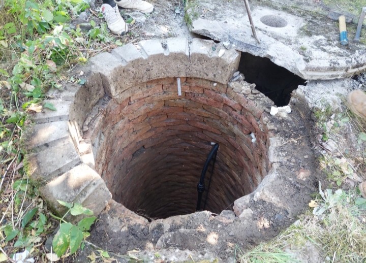 Pohled shora do cihlové studny s hadicí čerpadla uvnitř